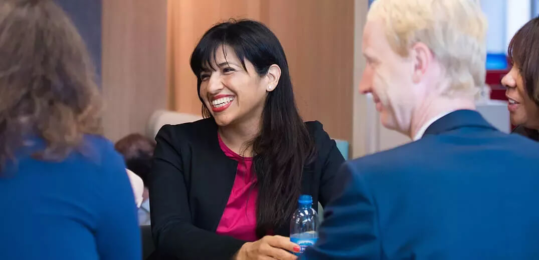 A group of professionals engaged in discussion at a conference, with a bottle of water on the table.
