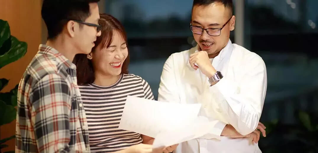 Three individuals are engaged in a discussion while reviewing documents in a well-lit indoor space.