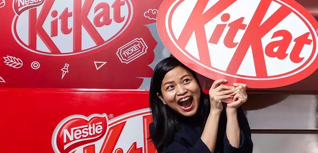 A person holds a large KitKat sign in front of vibrant red KitKat branding, creating a lively promotional atmosphere.